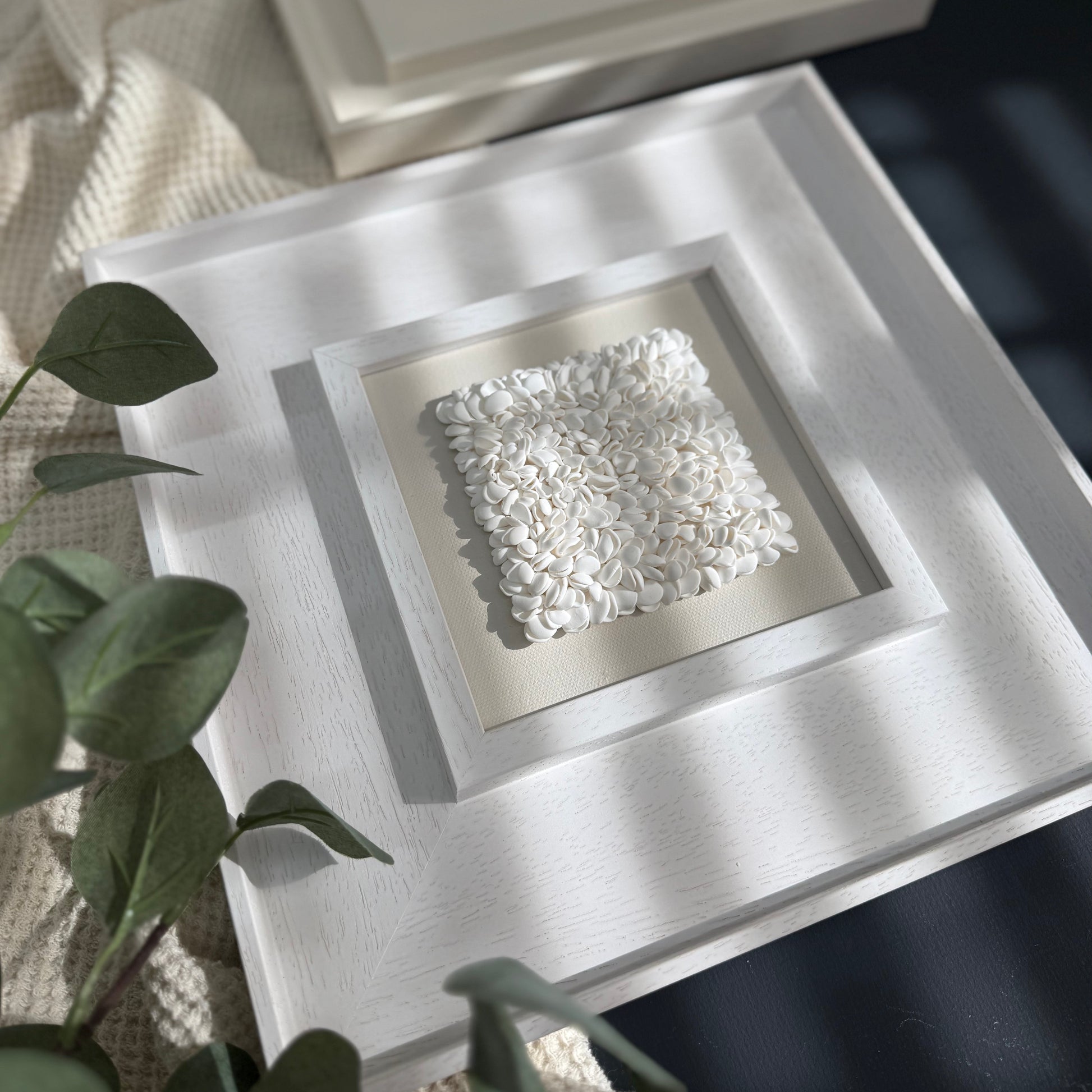 Decorative white stone in a square frame on a textured surface with a plant in the foreground.