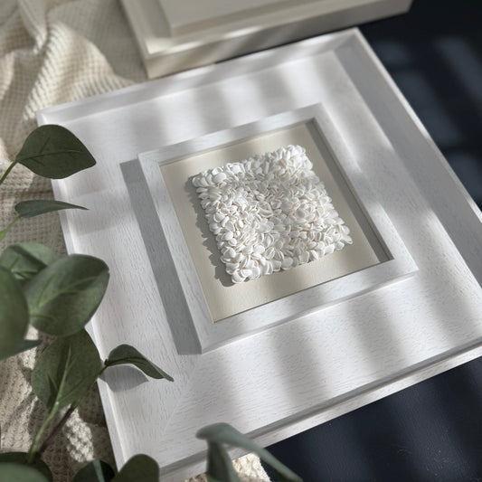 Decorative white stone in a square frame on a textured surface with a plant in the foreground.